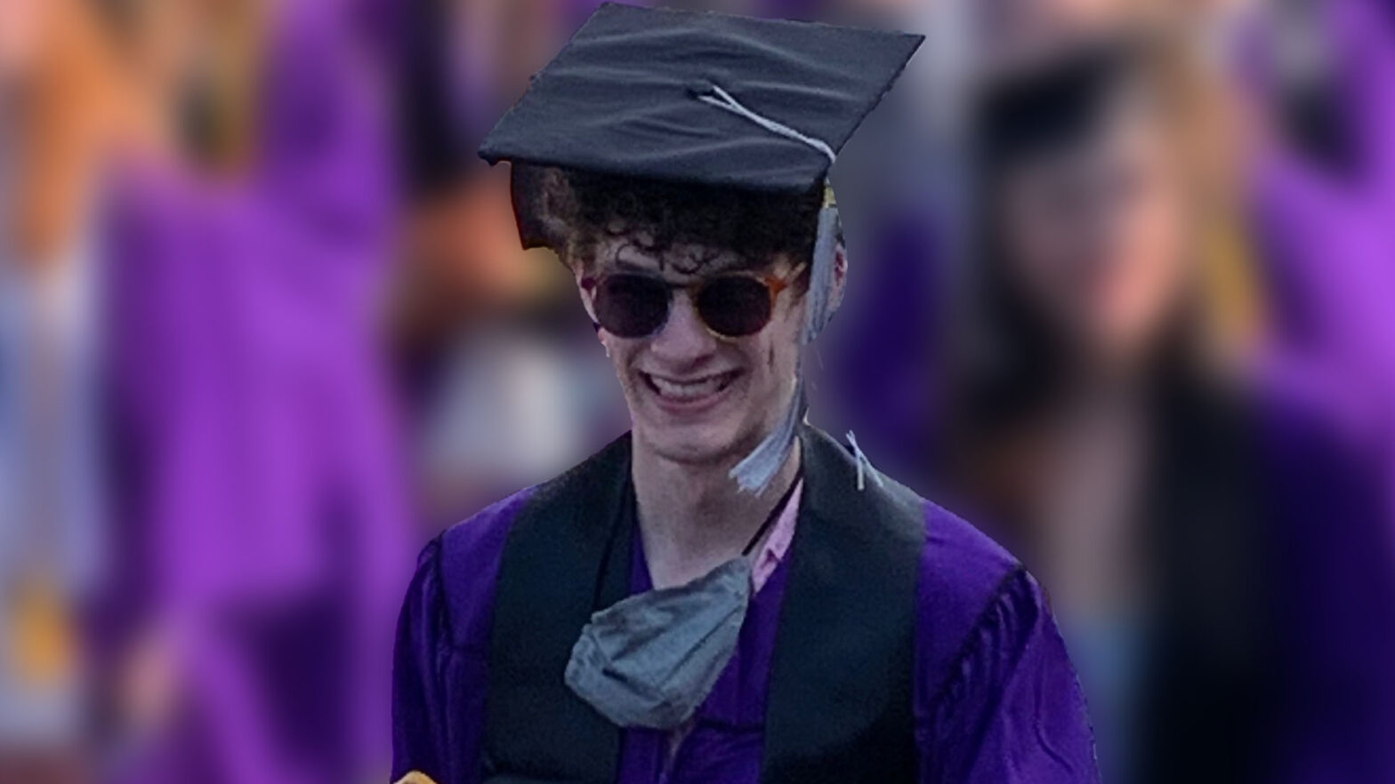 This image depicts Carter at his graduation from Northwestern. wearing a purple cap and gown and smiling at the camera while wearing sunglasses.